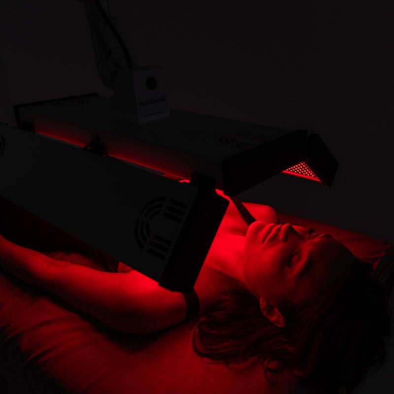 Model lying beneath the illuminated ApolloARC red light therapy panel during a full-body treatment session