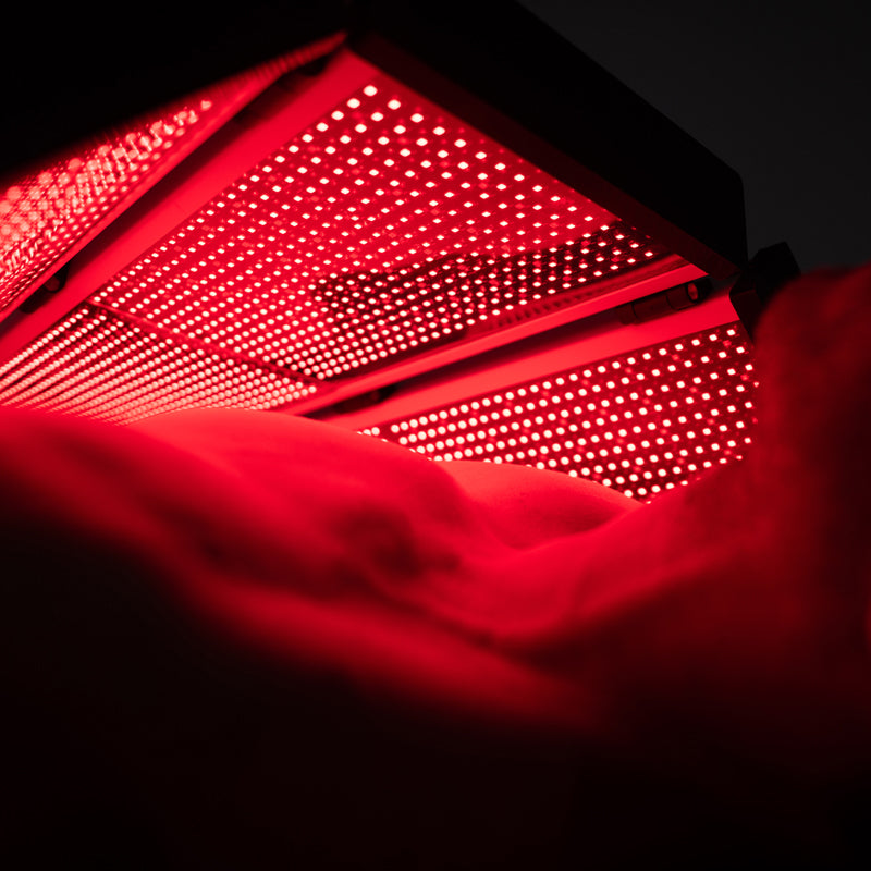 Close-up view of the ApolloARC red light therapy panel illuminated beneath a model, showing LED arrays and bright red light glow
