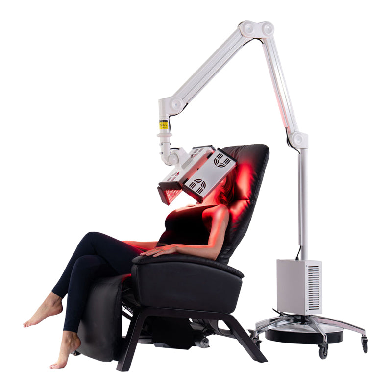 Model receiving facial treatment with the ApolloGlow red light therapy panel positioned on an adjustable arm over a reclining chair