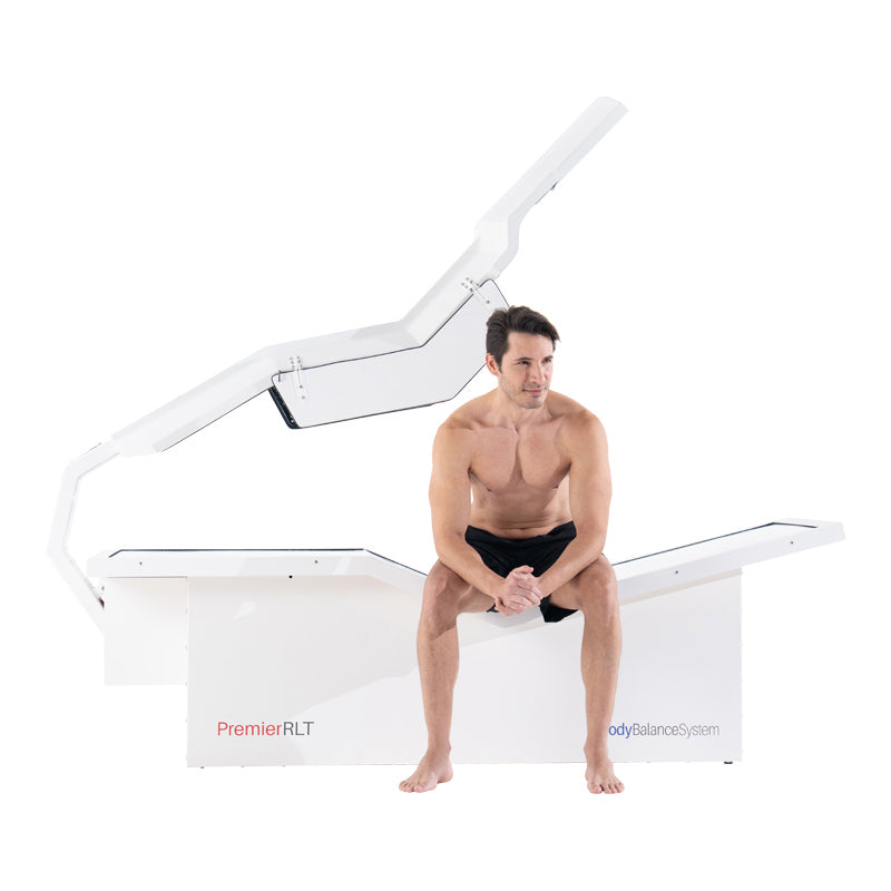 Man sitting on Body Balance System PremierRLT zero gravity red light therapy bed side profile with canopy open on white background