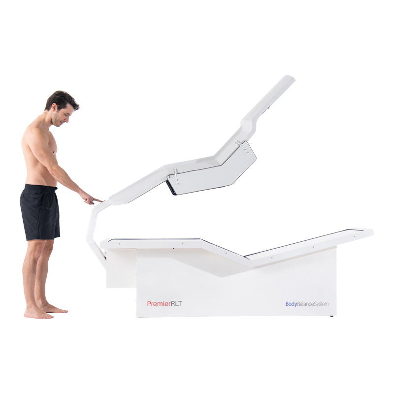 Man demonstrating Body Balance System PremierRLT zero gravity red light therapy bed with canopy open on white background