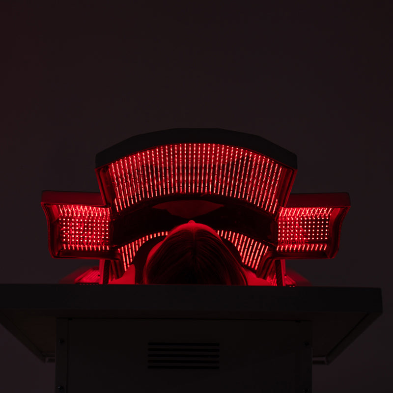 Woman using Body Balance System PremierRLT red light therapy bed with canopy closed LEDs illuminated in dark setting