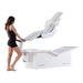 Woman demonstrating Body Balance System PremierRLT zero gravity red light therapy bed with canopy open on white background