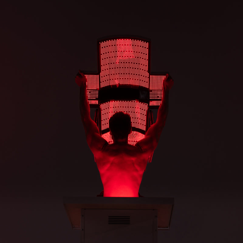 Man using Body Balance System PremierRLT red light therapy bed with canopy LEDs illuminated in dark setting