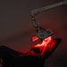 ApolloGlow facial red light therapy panel positioned on adjustable arm during a client treatment session.