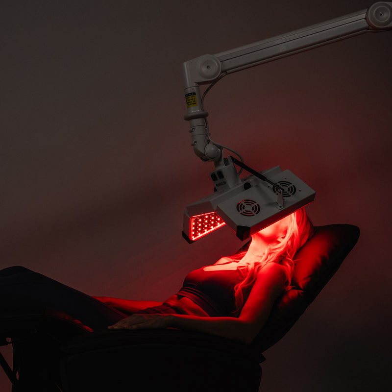 ApolloGlow facial red light therapy panel positioned on adjustable arm during a client treatment session.