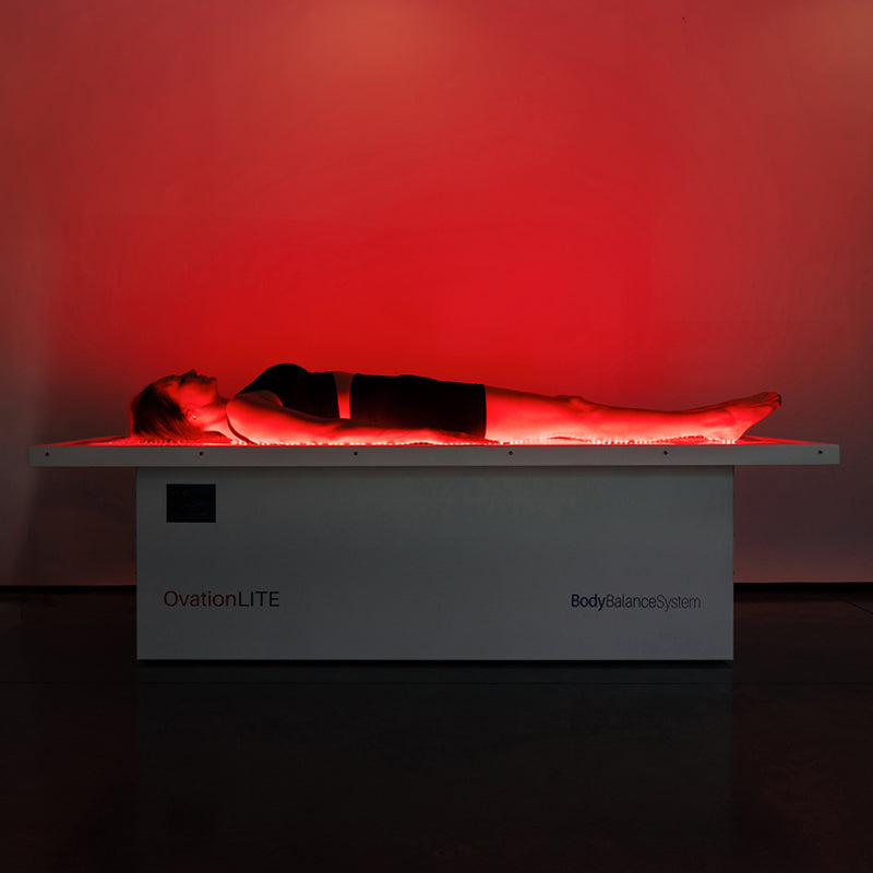 Female lying flat on Body Balance System OvationLITE red light therapy bed with full-body LED illumination