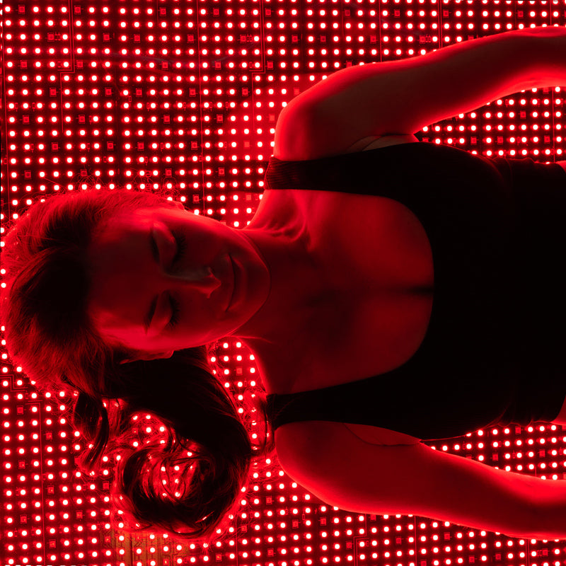 Female model lying on Body Balance System OvationLITE red light therapy bed with LEDs illuminated