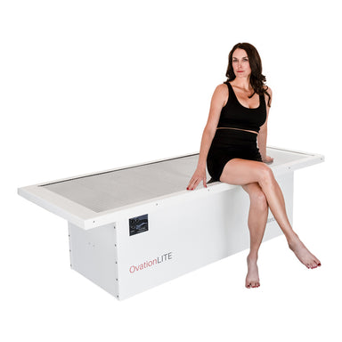 Female model sitting cross legged on Body Balance System OvationLITE red light therapy bed whit background powered off