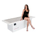 Female model sitting cross legged on Body Balance System OvationLITE red light therapy bed whit background powered off