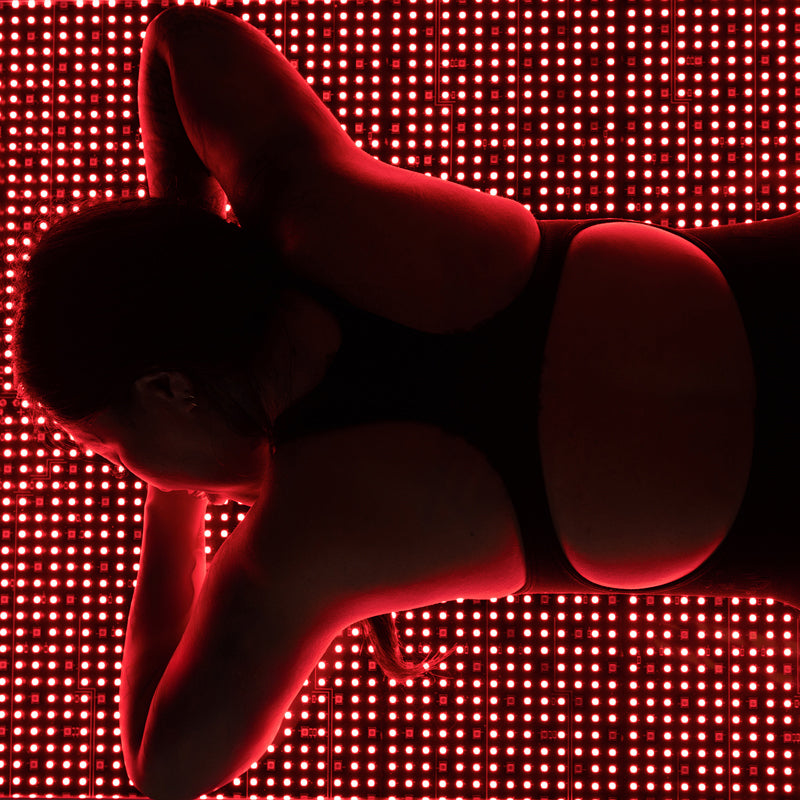 Female model lying face down on Body Balance System OvationLITE red light therapy bed with LEDs illuminated, overhead view