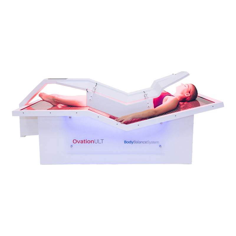 Body Balance System OvationULT Red Light Therapy Bed – front view powered on with canopy fully closed, female model inside during active red light therapy session for full-body rejuvenation.