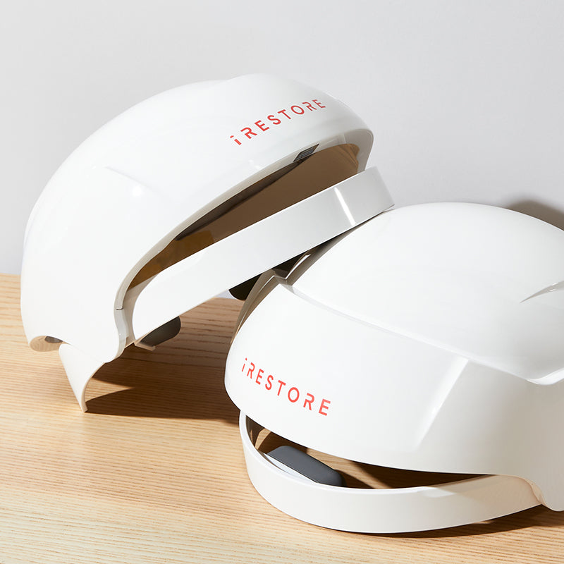 two iRestore Essential laser hair growth helmets stacked against each other on counter top white background angle view